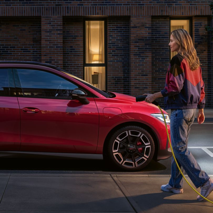Oseba se približa rdečemu VW ID-ju. Polo GTI, parkiran ob strani z DC polnilnim kablom.