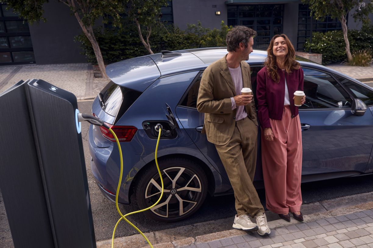 Eine Frau und ein Mann lehnen an einem VW ID.3 Neo, der am Straßenrand lädt