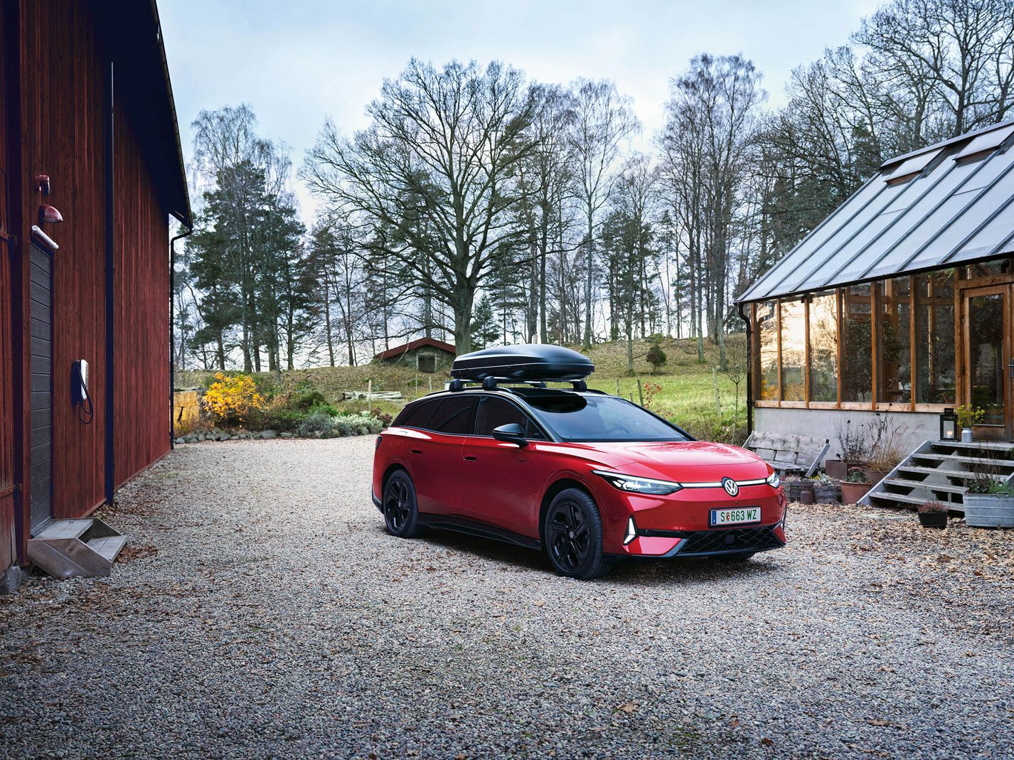 VW ID.7 GTX Tourer s strešnim kovčkom, parkiran med dvema hišama.