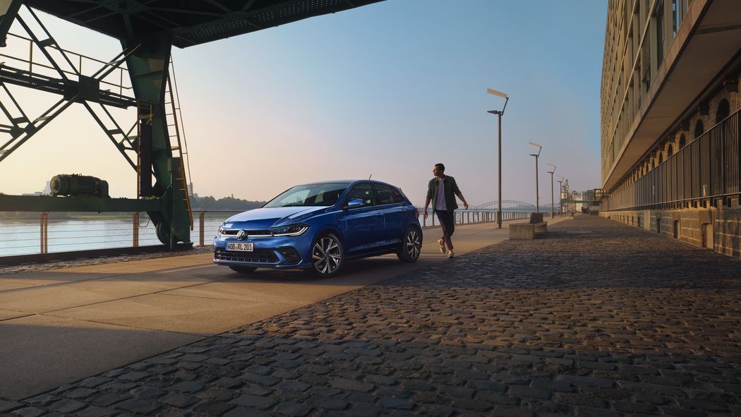 Moški gre mimo modrega VW Polo R-Line, parkiranega na promenadi