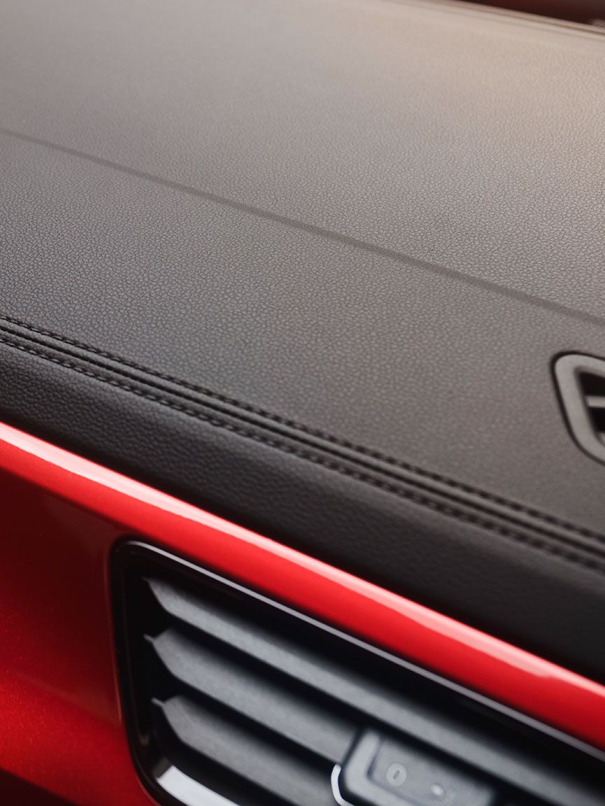 Detajlni posnetek okrasnih šivov na armaturni plošči VW T-Roc Cabrioleta z rdečimi dekorativnimi elementi.