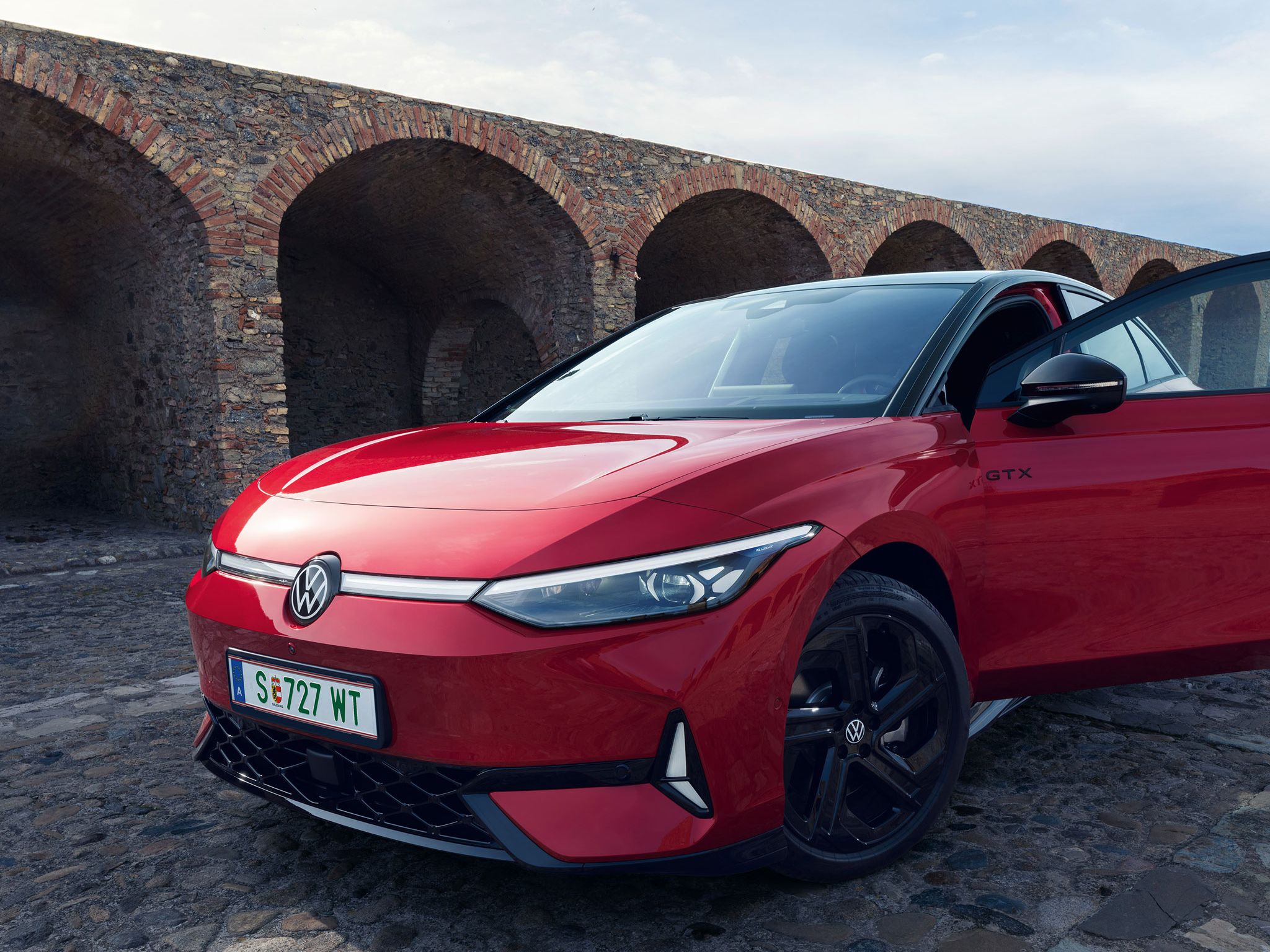 Rdeč Volkswagen ID.7 GTX stoji pred staro kamnito zgradbo z oboki.